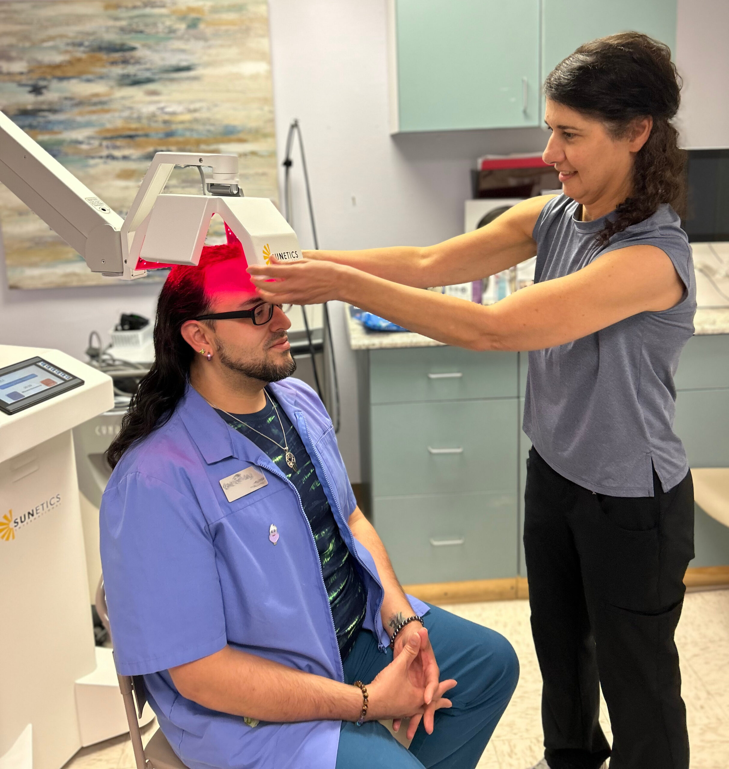 Photo of a patient sitting under a laser being adjusted by a medical professional 